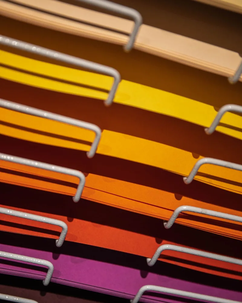 Estantería de papeles de color ordenados por tono, del crema al magenta, vistos en diagonal